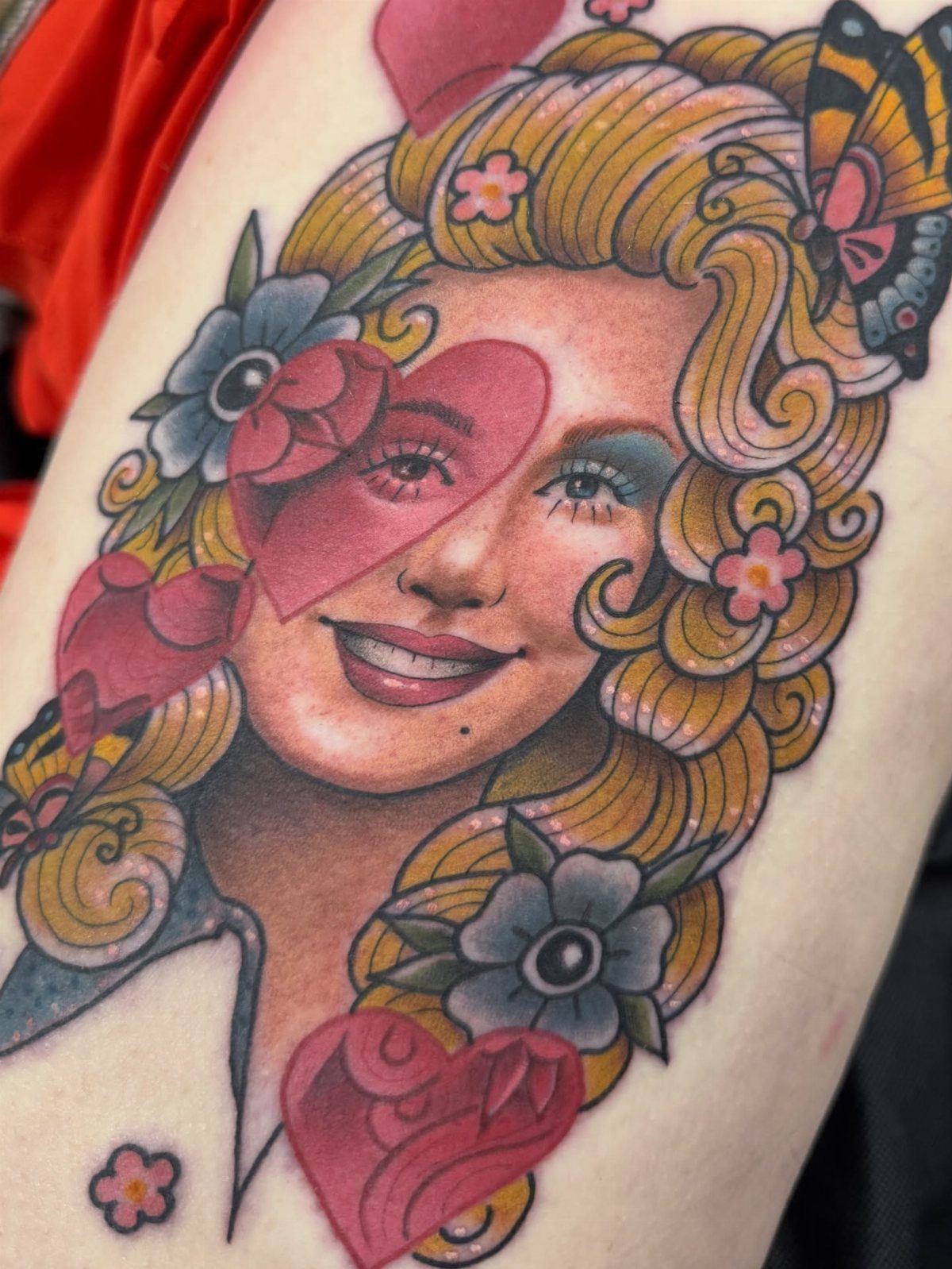 Dolly Parton portrait tattoo with pastel pink hearts and blue flowers on skin
