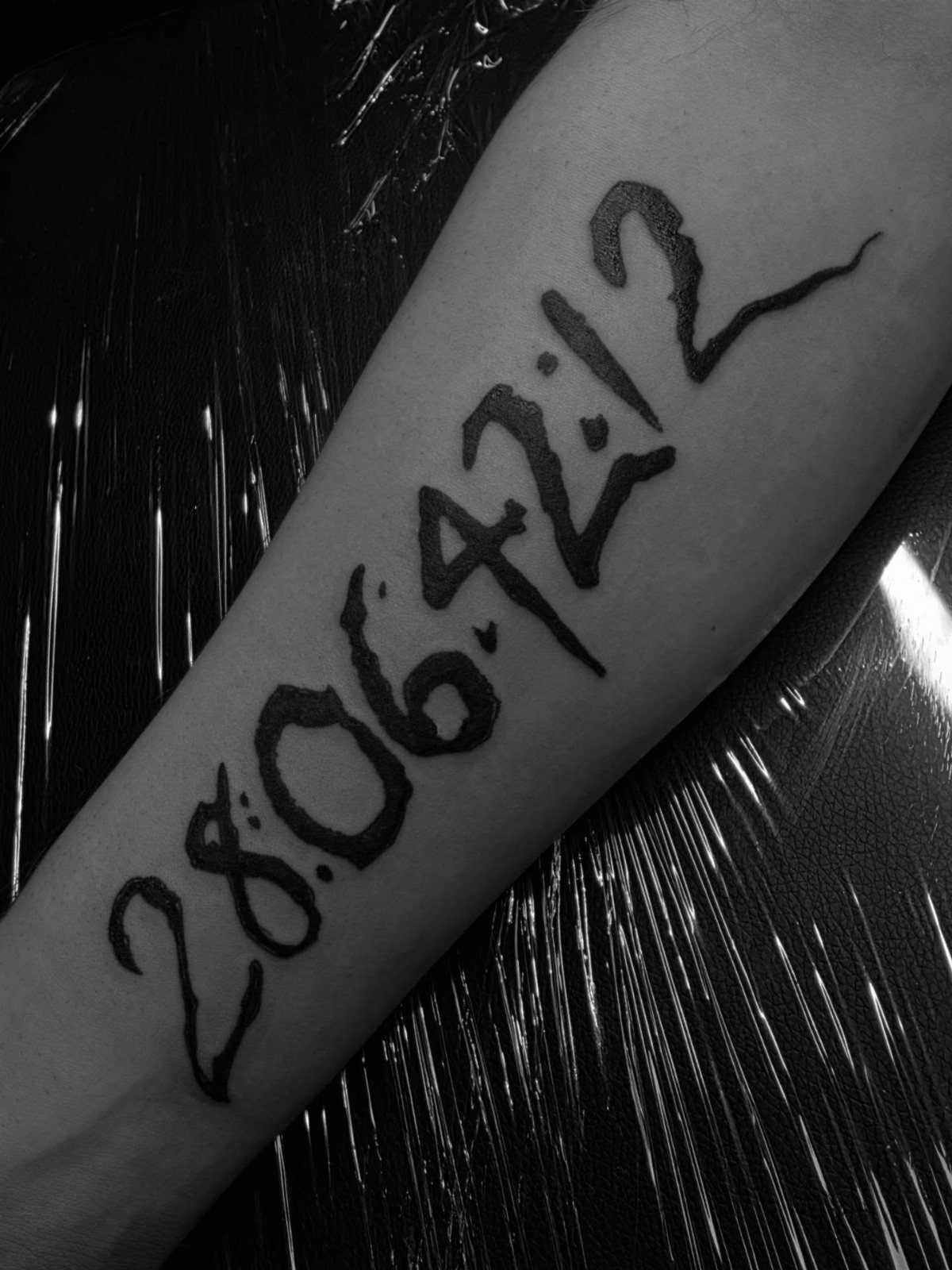 Tattoo of the numbers 28:06:42:12 in black ink on a person's arm.