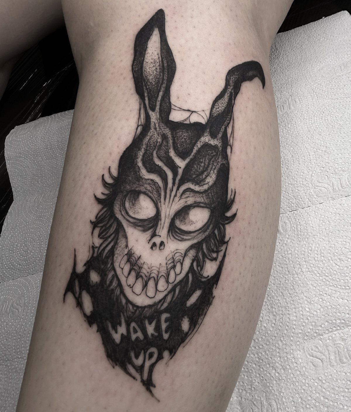 Skeletal rabbit tattoo on a leg with the words Wake Up below it.