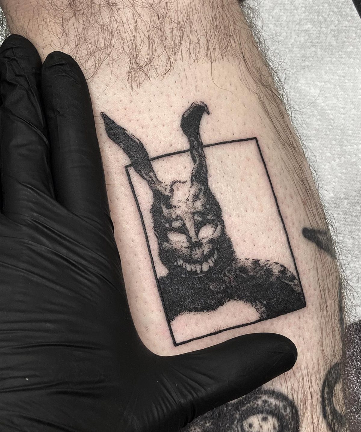 Donnie Darko rabbit tattoo on a leg with a gloved hand nearby