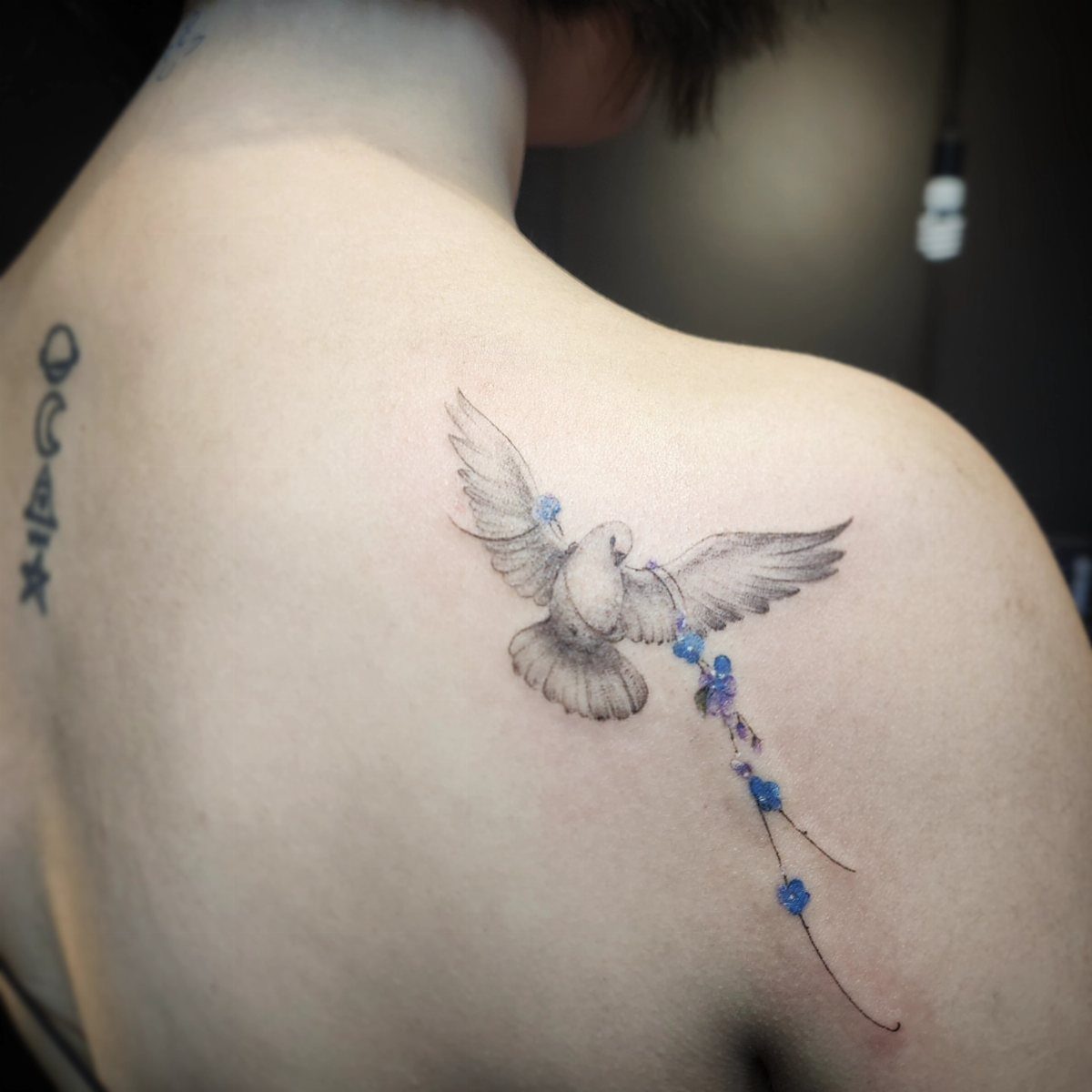 Dove tattoo with blue flowers on a person's shoulder and upper back.