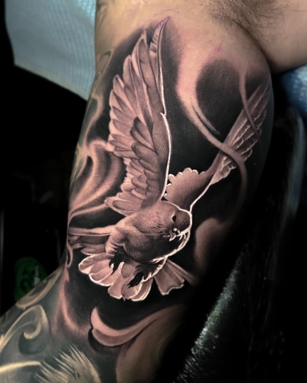 Flying dove tattoo with detailed shading and white highlights on a person's arm.