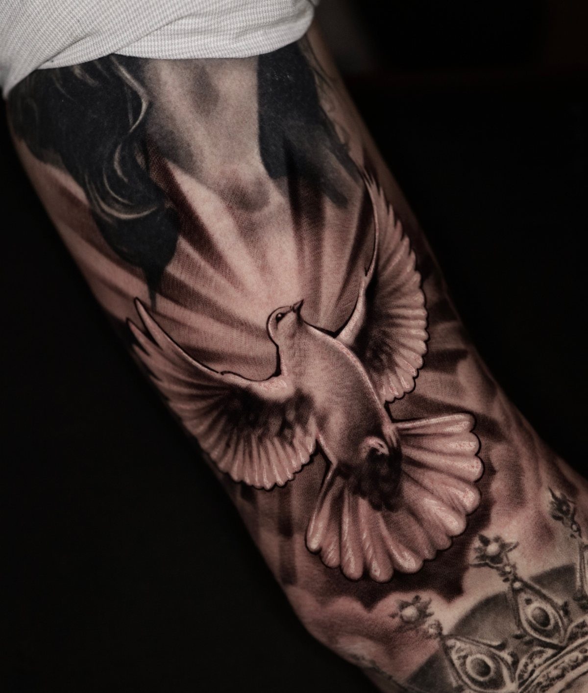Dove tattoo with radiating light beams and clouds on a person's arm.