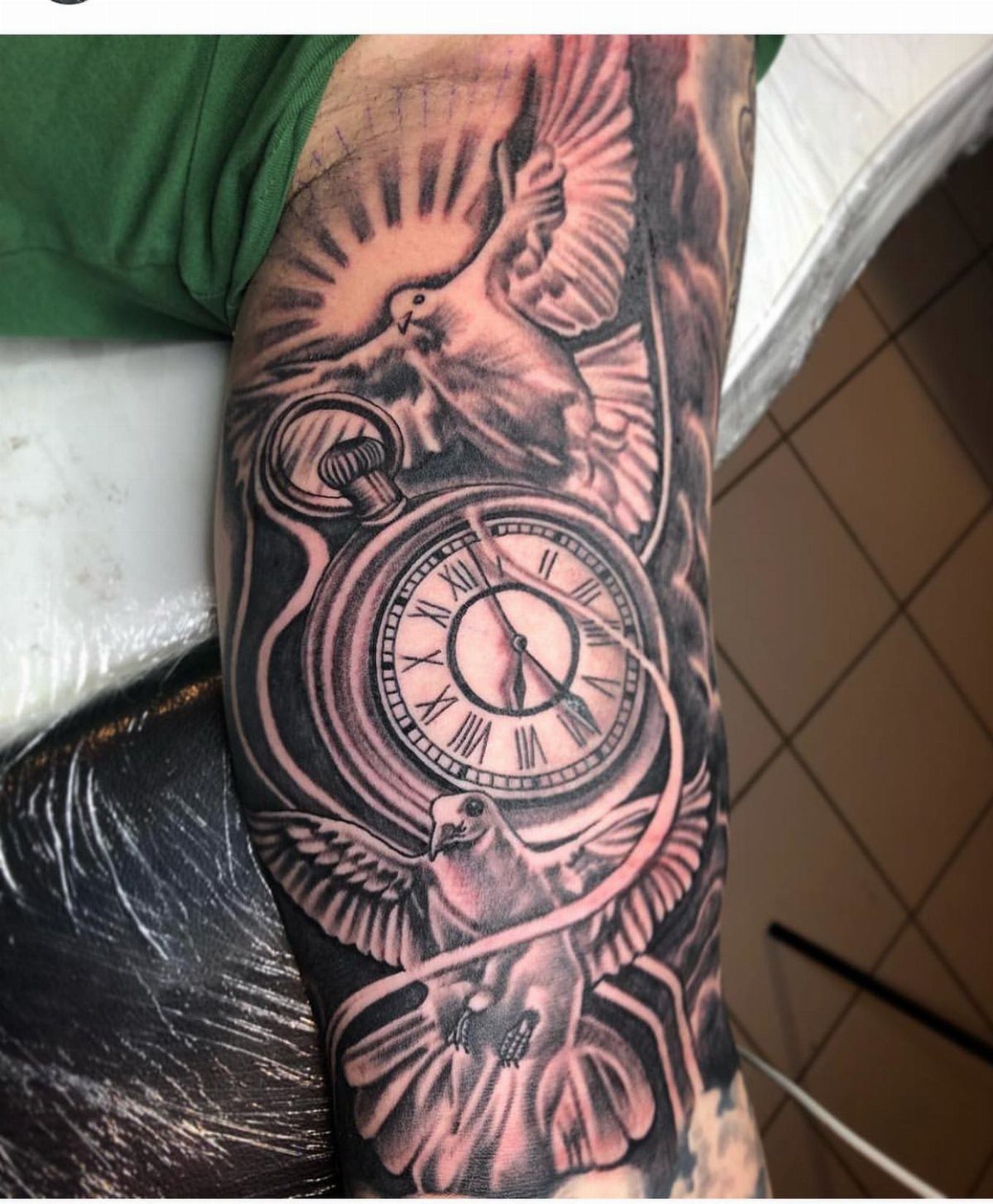Two doves flying around a pocket watch in a black and grey arm tattoo.
