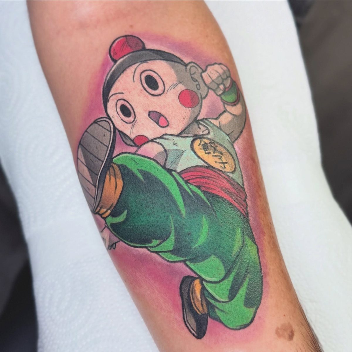 Chiaotzu tattoo on an arm featuring the character in a green outfit and red cheeks.