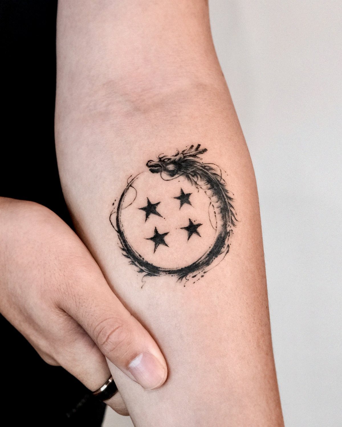 Four star dragon ball tattoo with a dragon wrapped around it on a forearm