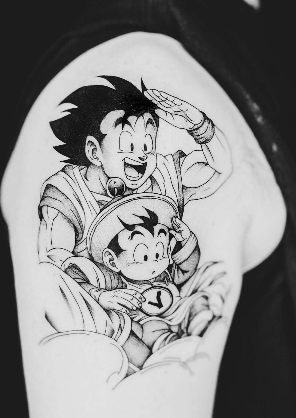 Goku and Goten tattoo in black and grey ink on an upper arm.