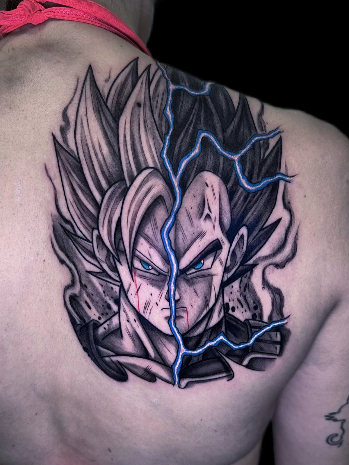 Split face tattoo of Goku and Vegeta on a shoulder with blue lightning.