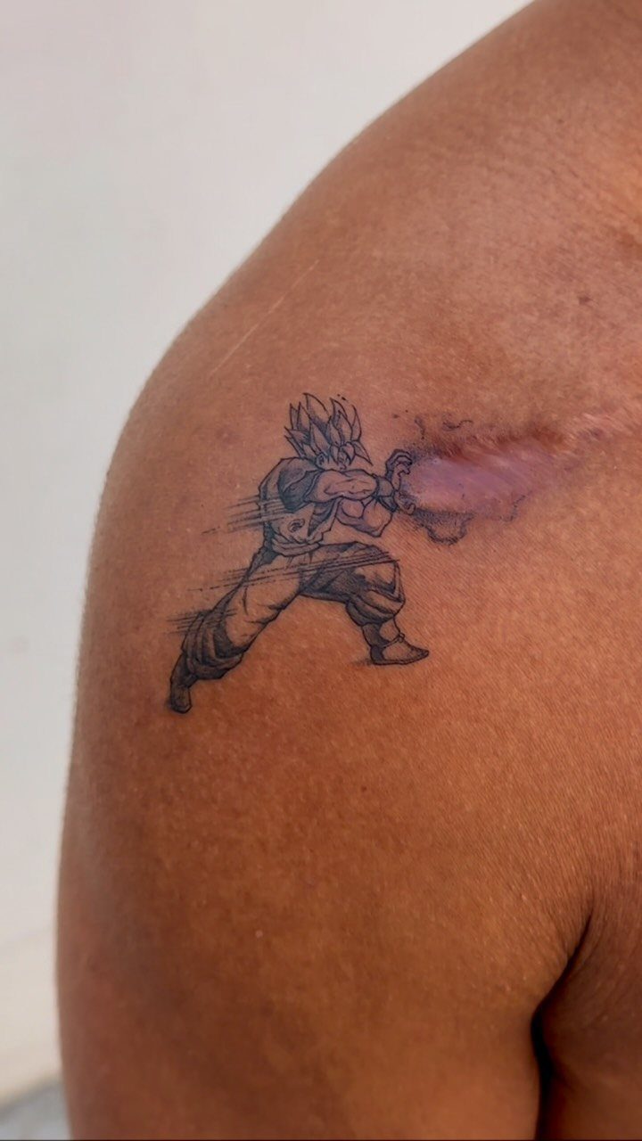 Goku tattoo on a shoulder firing a purple Kamehameha energy blast.