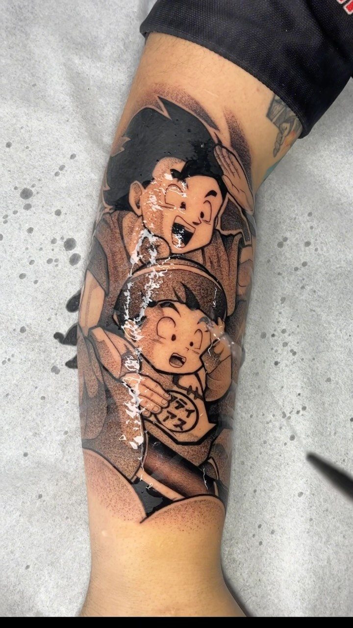 Goku and young Gohan tattoo on a forearm in black and grey ink