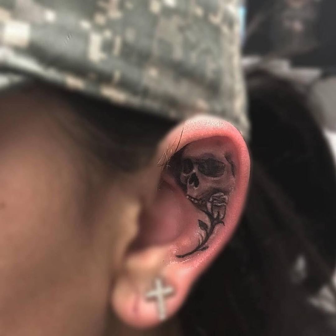 Realistic grey and black ink skull tattoo with a rose on an ear