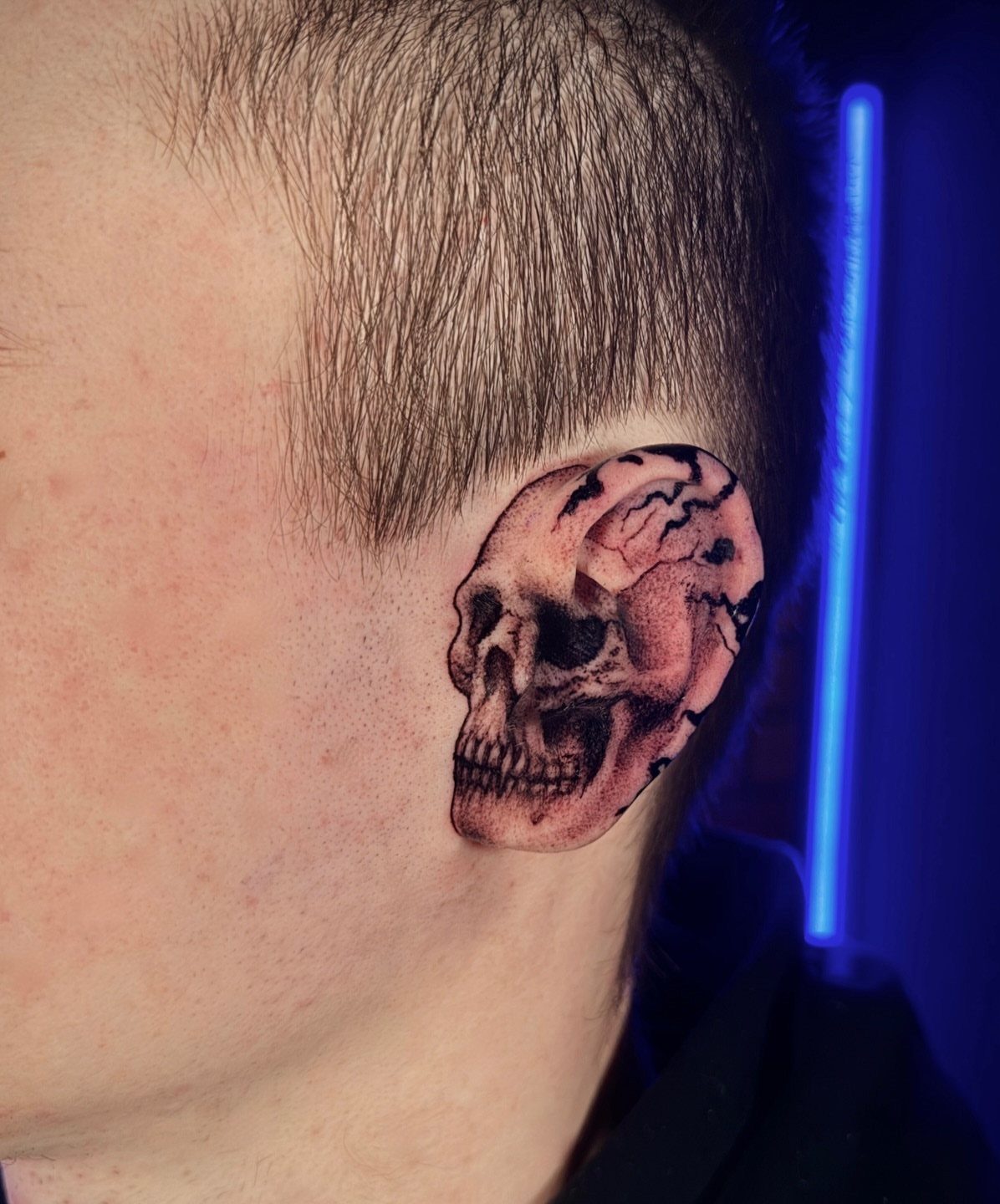 Skull tattoo on a human ear, blending the skull's anatomy with the ear's shape.