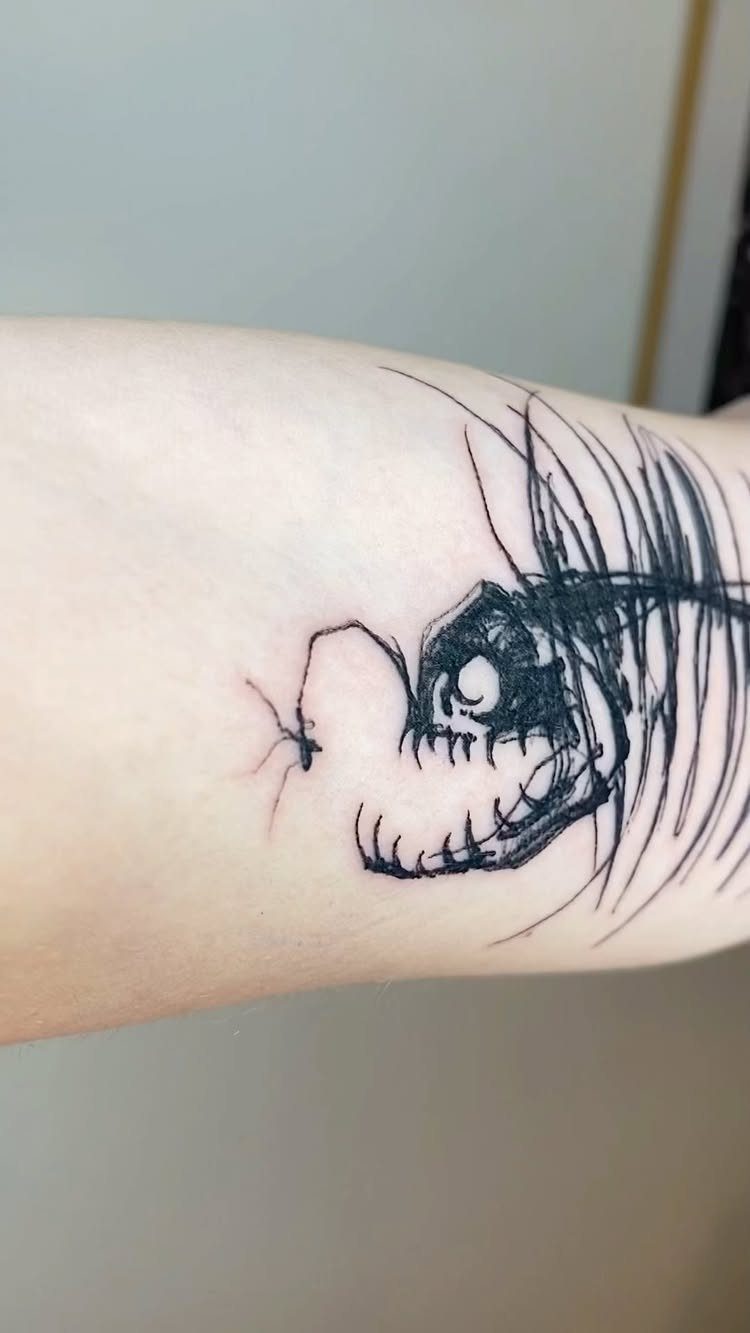Anglerfish skeleton tattoo with sharp teeth and a lure on pale skin