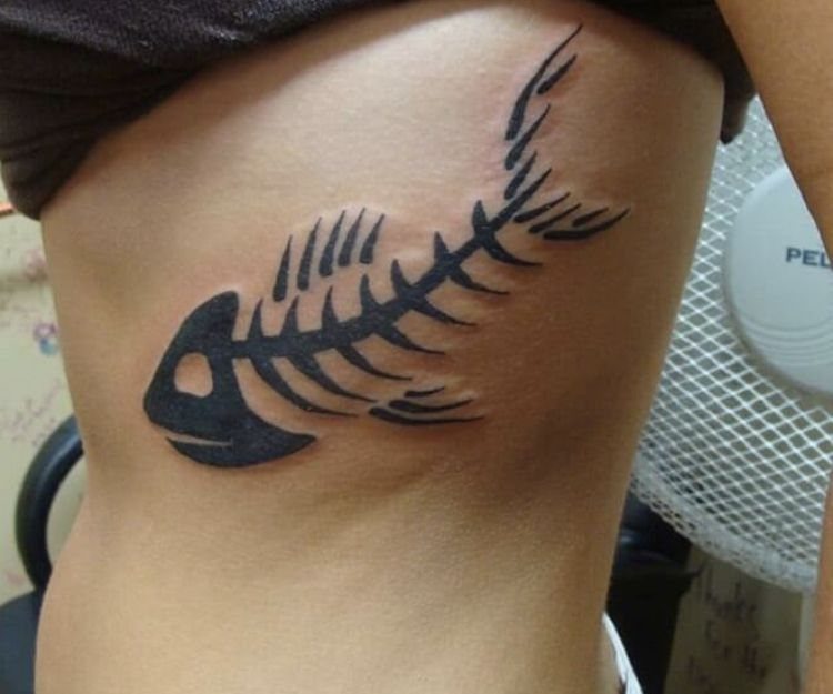 Tribal fish skeleton tattoo in black ink on a person's side torso