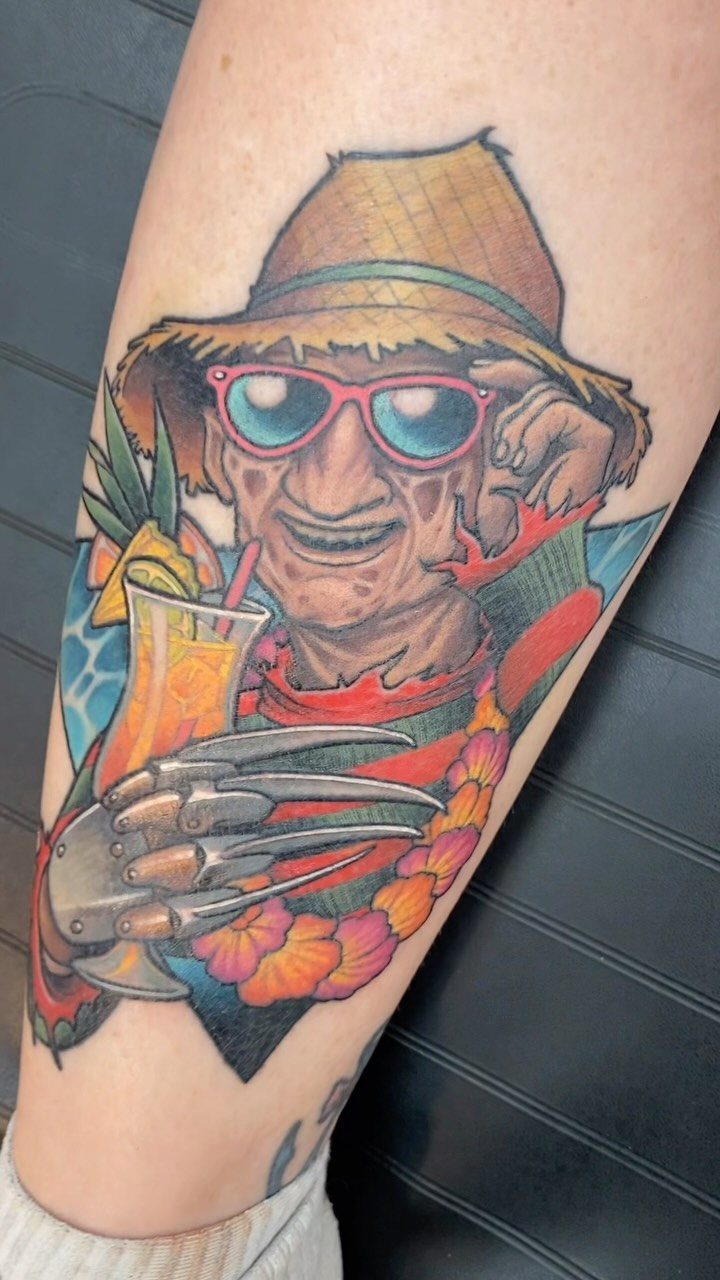 Freddy Krueger tattoo wearing a straw hat and floral lei holding a tropical drink