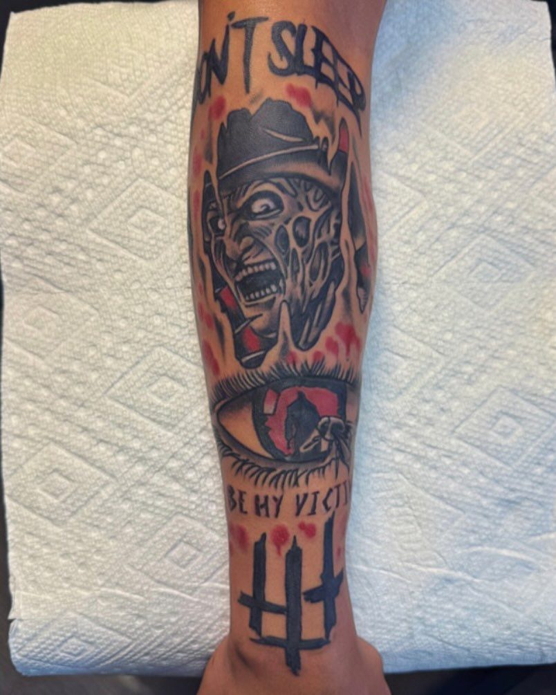 Freddy Krueger portrait tattoo with red blood splatter and horror themed text on arm
