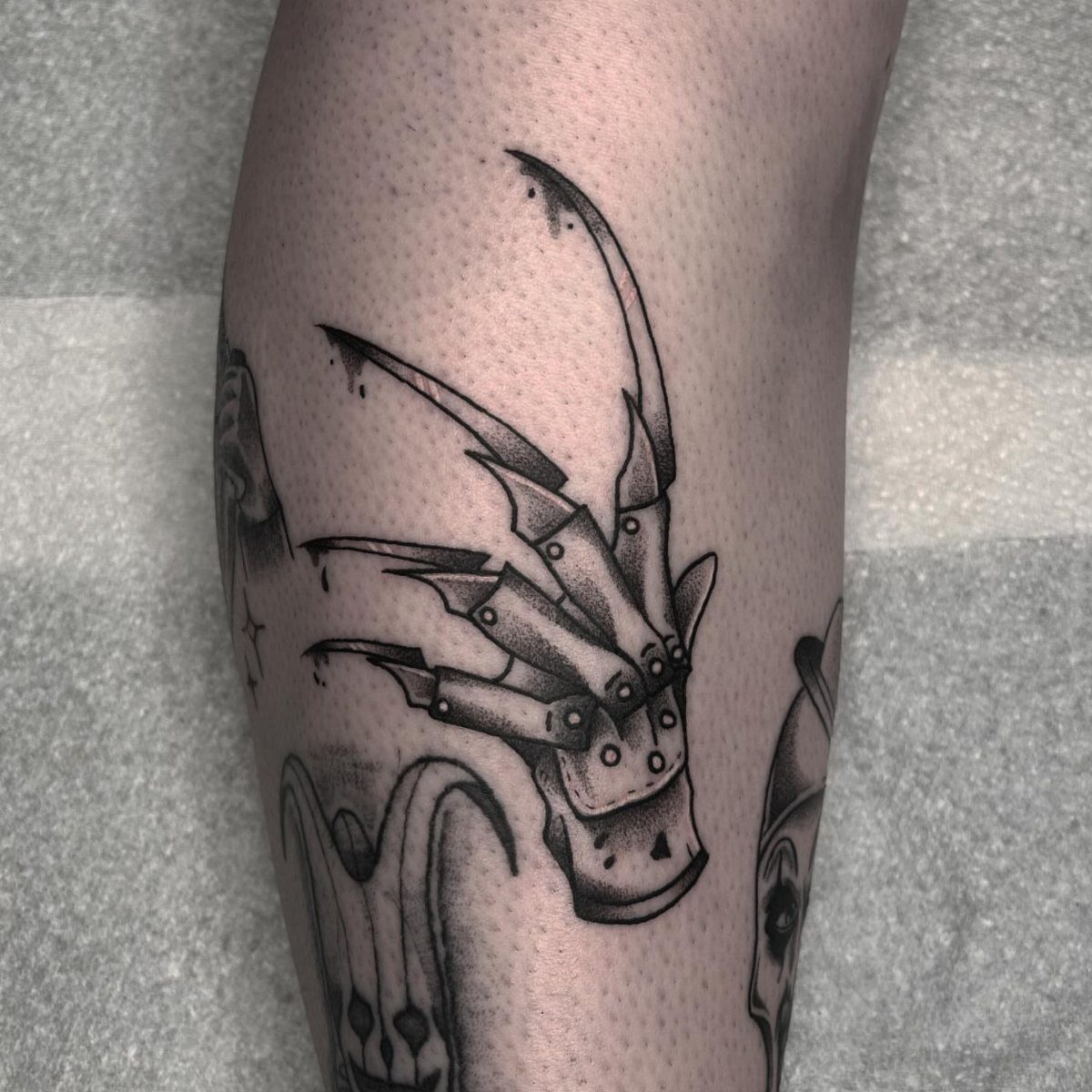 Freddy Krueger's bladed glove tattoo in black and grey ink on skin.