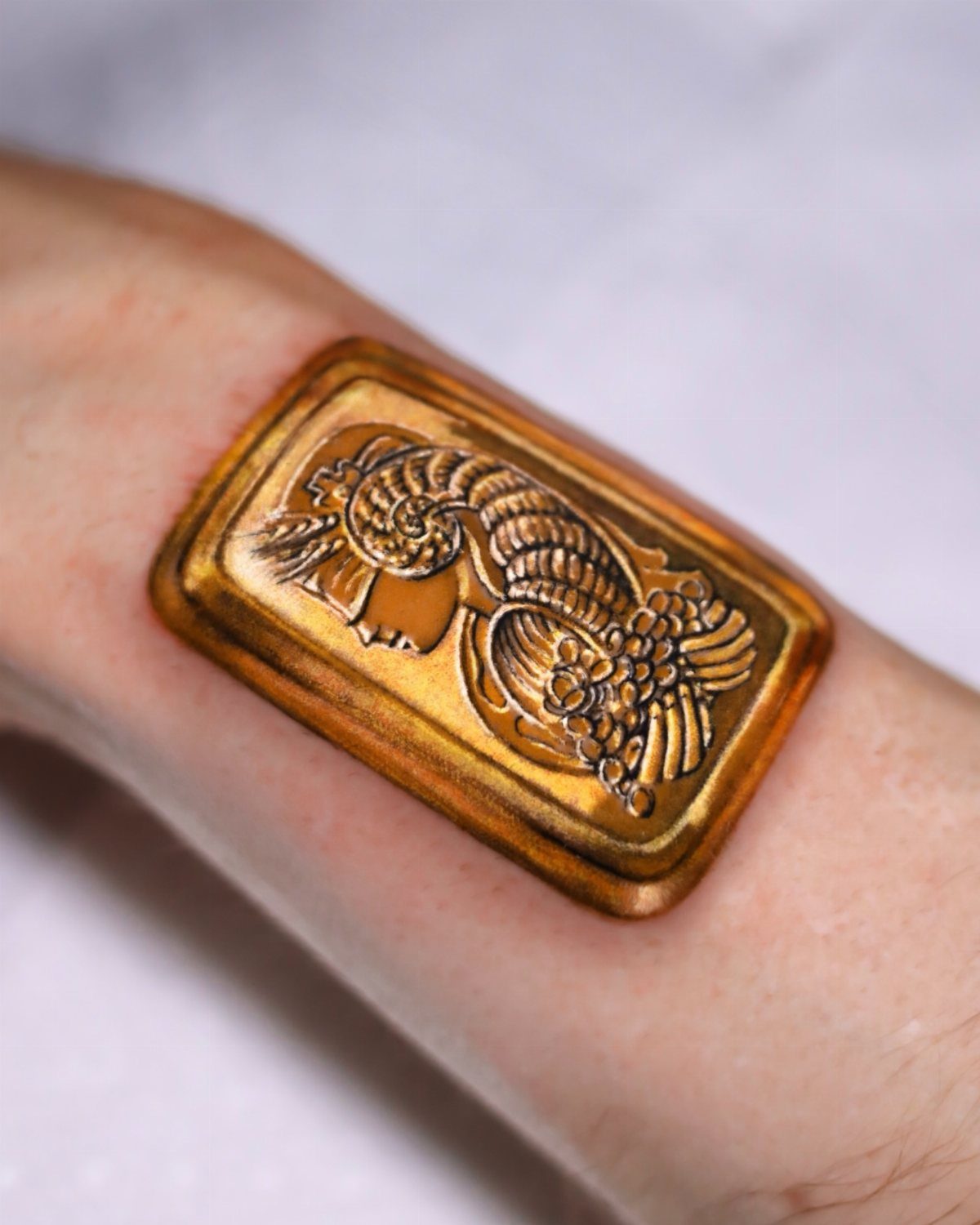 Gold metallic 3D tattoo of a classical woman's profile on a person's arm.