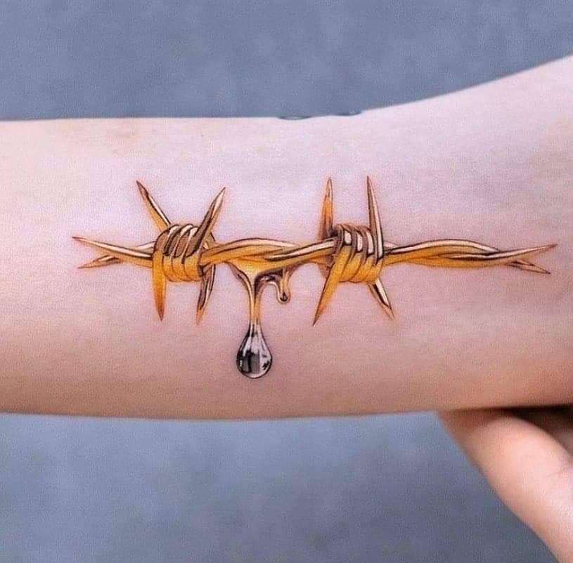 Gold barbed wire tattoo on a forearm with a realistic liquid droplet