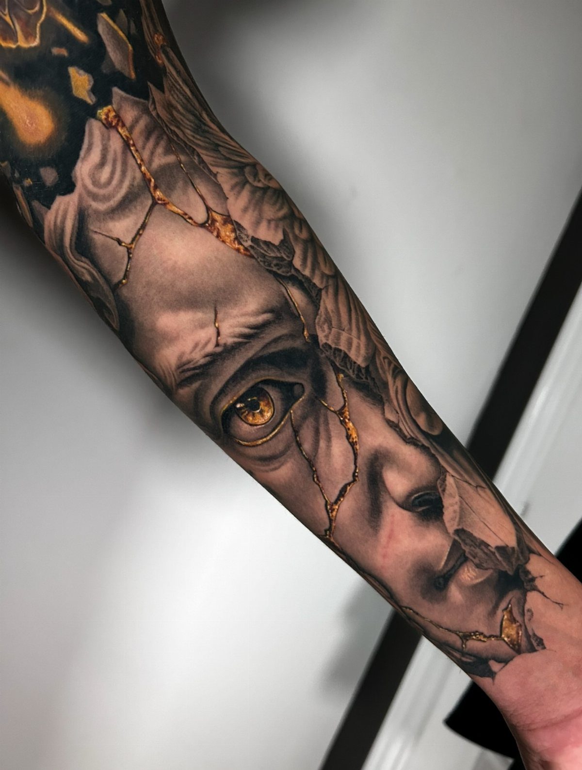 Tattoo of a cracked stone face with shimmering gold ink in the fissures.