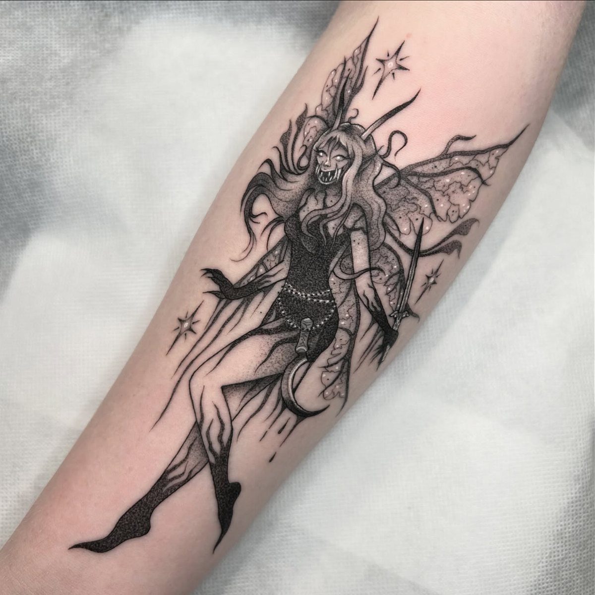 Gothic fairy tattoo with a skull face and tattered wings on an arm.