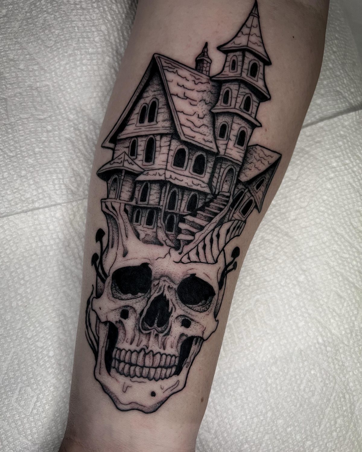 Haunted house tattoo perched on a skull on a person's arm.