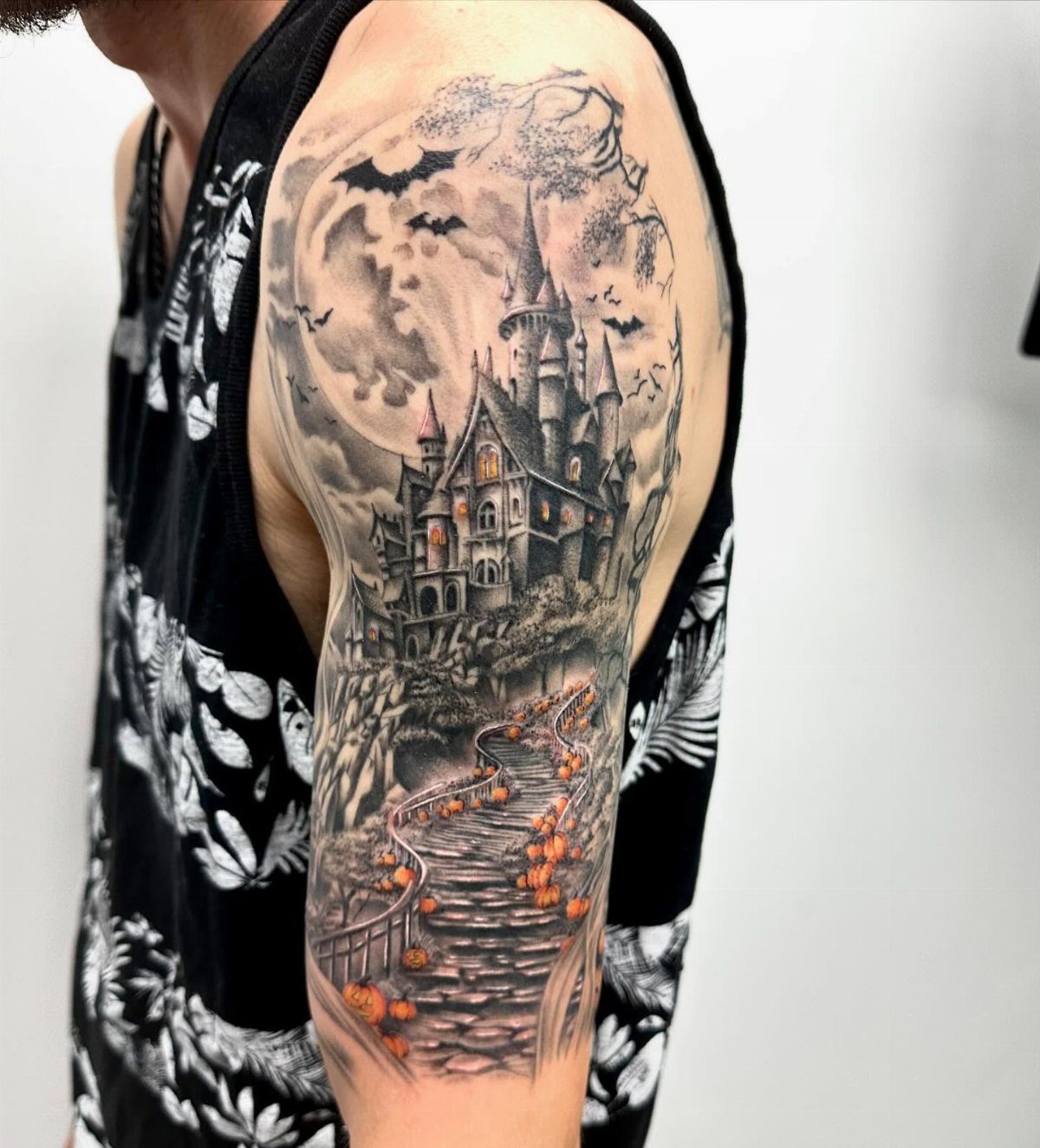 Gothic haunted house tattoo on an arm with a large moon and pumpkins.