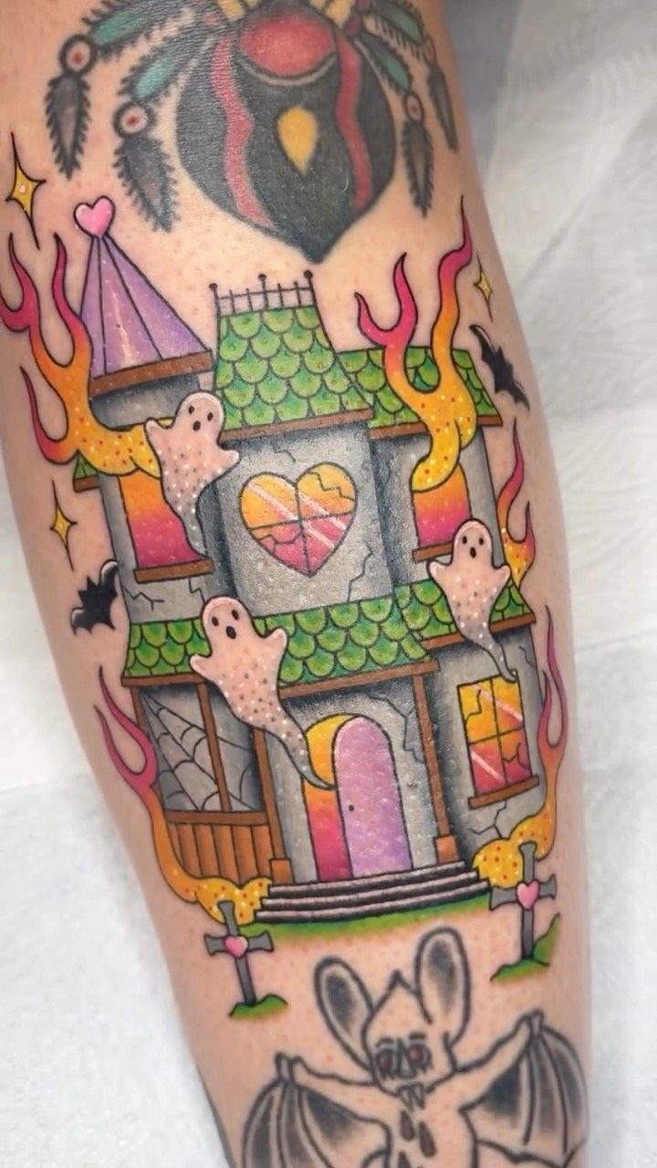 Neo-traditional haunted house tattoo with ghosts, flames, and colorful details on skin.