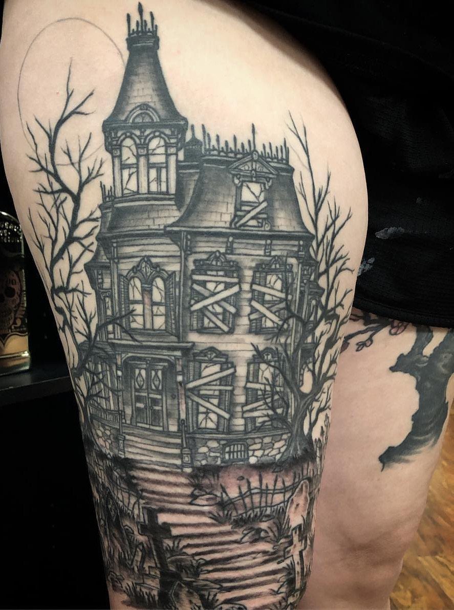 Haunted house tattoo on a thigh featuring a spooky graveyard and bare trees.