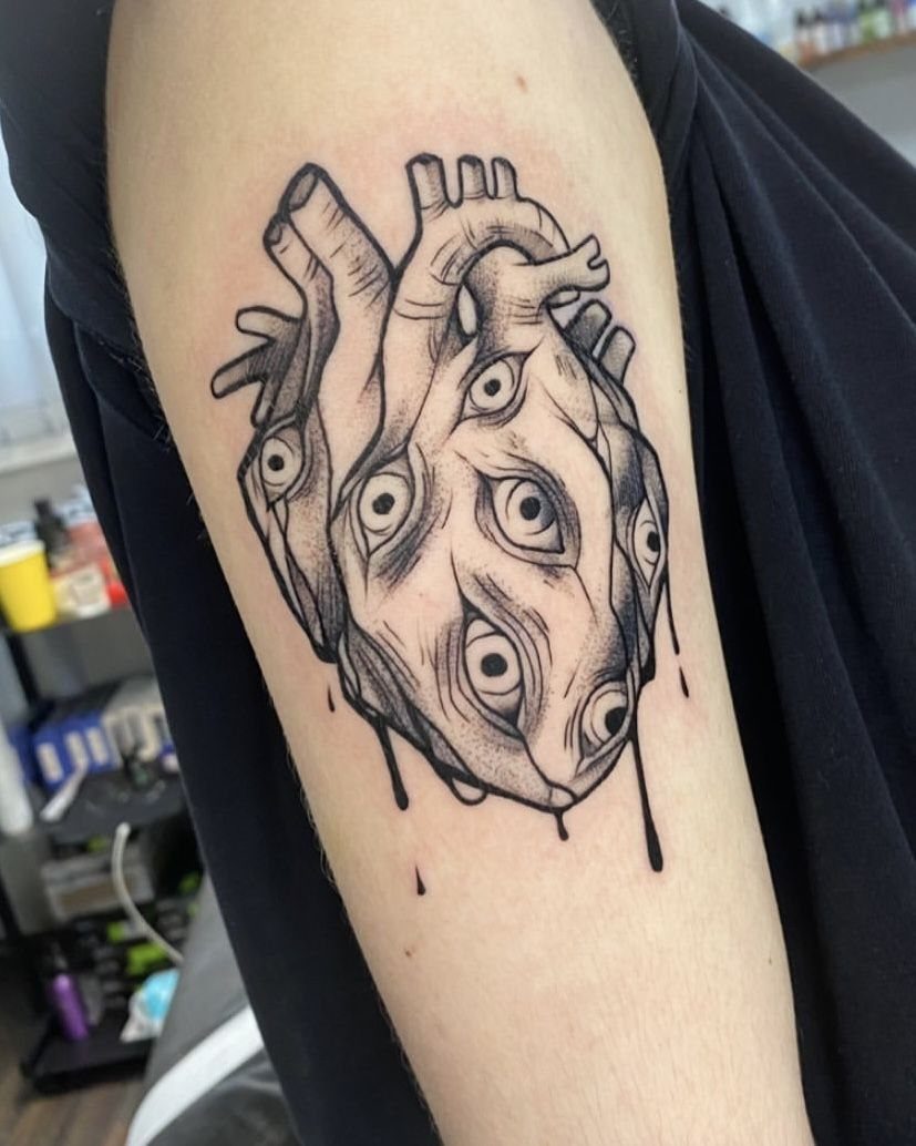 Anatomical heart tattoo with multiple eyes and dripping ink on an arm.