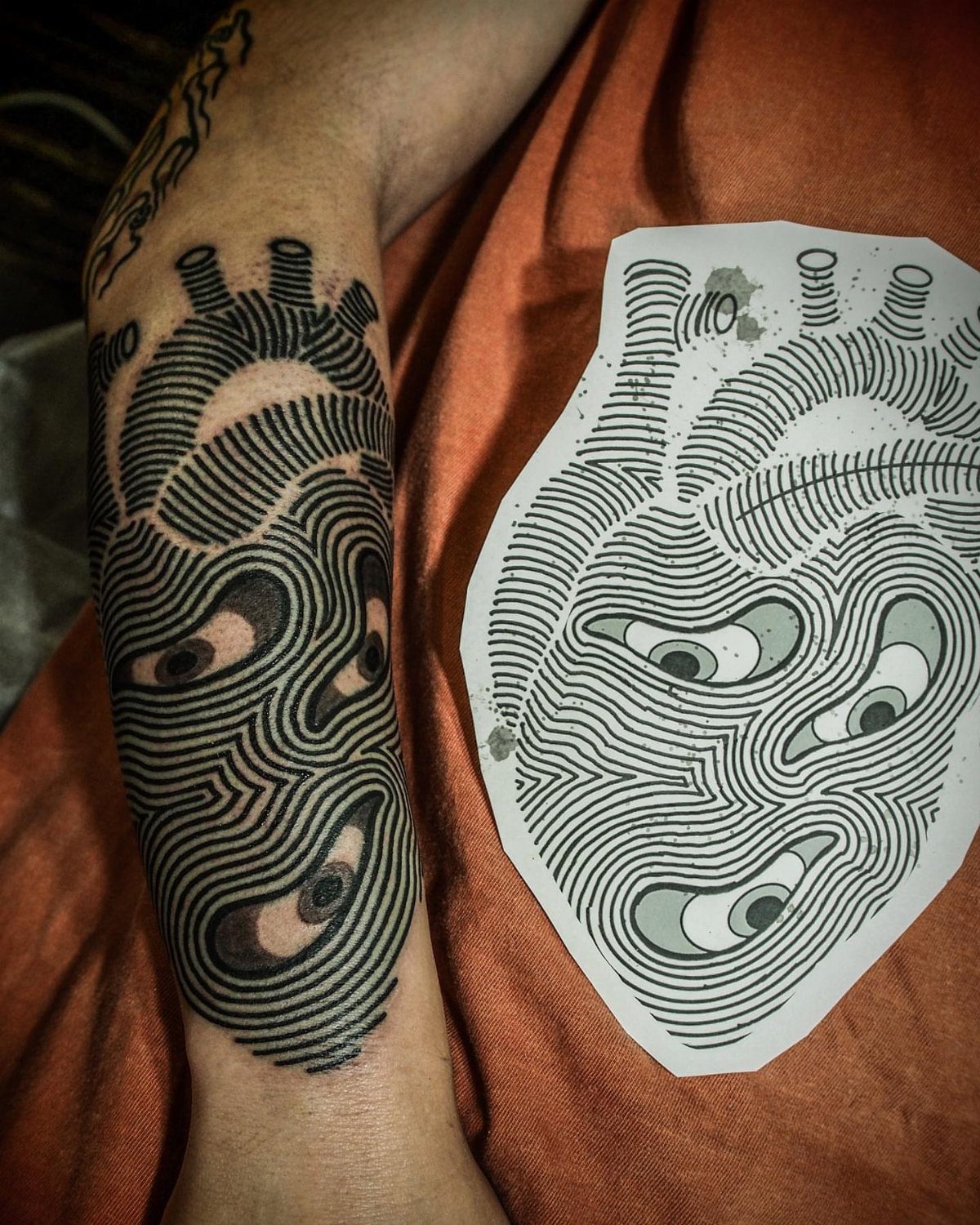 Black ink heart tattoo with multiple eyes and optical illusion lines on a forearm