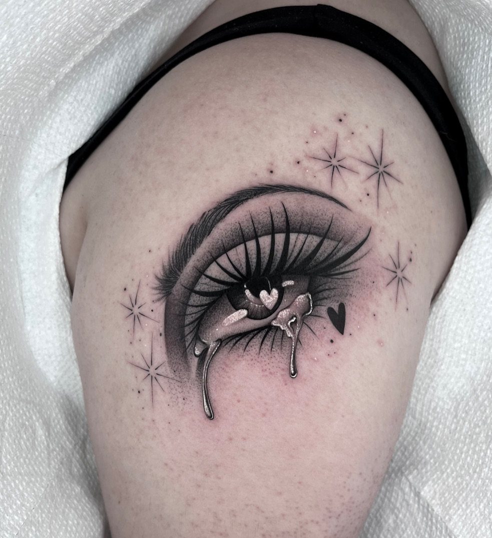 Tattoo of a crying eye with a heart pupil and small surrounding stars.