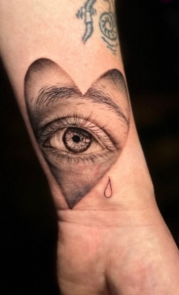 Heart shaped tattoo containing a realistic eye with a small teardrop beside it