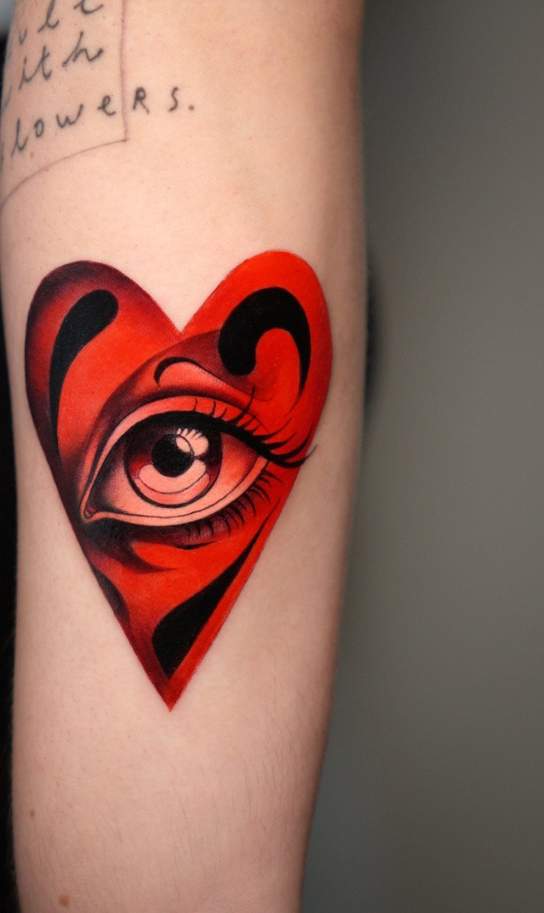 Red heart tattoo with a detailed eye in the center on an arm