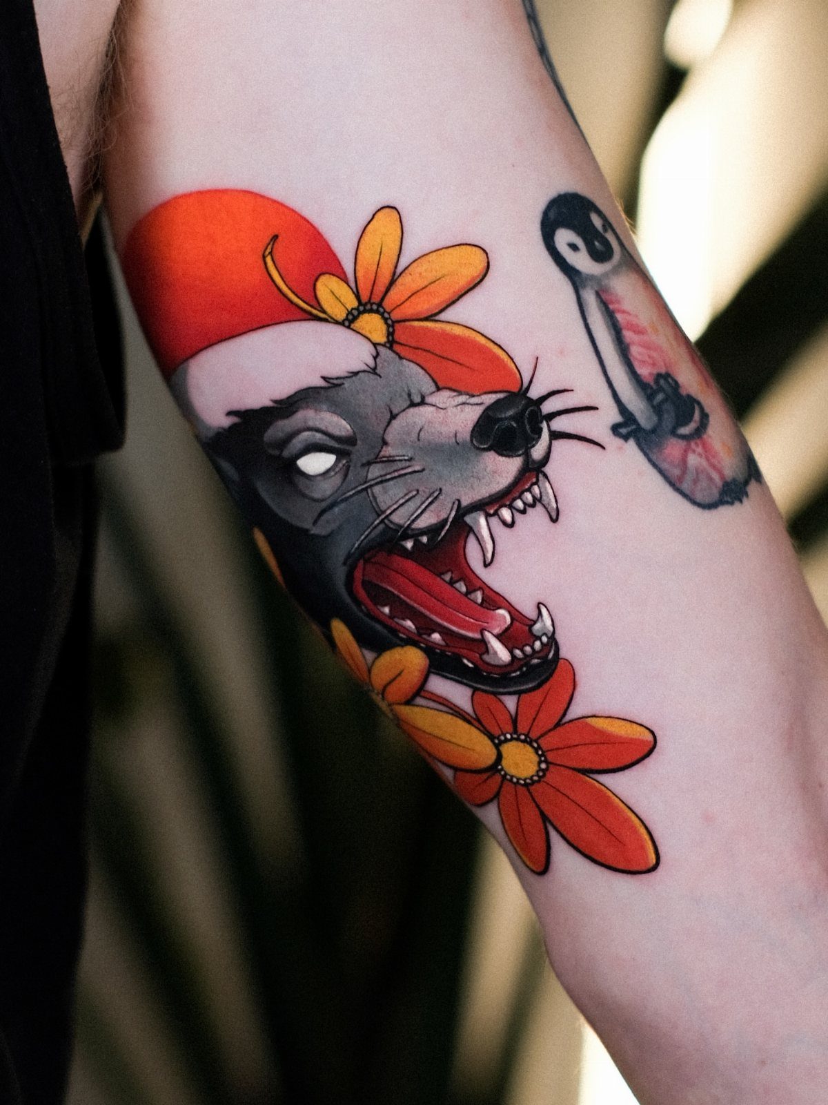 Honey badger head tattoo with orange flowers on a person's arm.