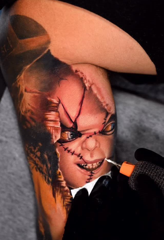 Chucky portrait tattoo on an arm being finished by a tattoo artist