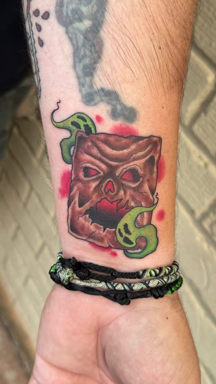 Necronomicon book tattoo with a demonic face and green smoke on a wrist