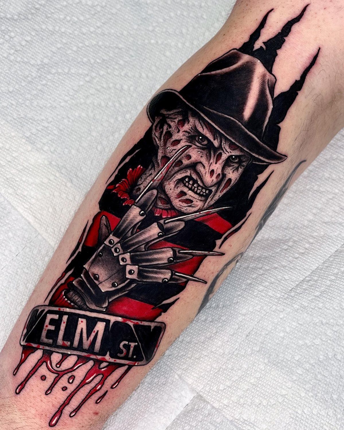 Freddy Krueger tattoo on an arm featuring his clawed glove and Elm Street banner
