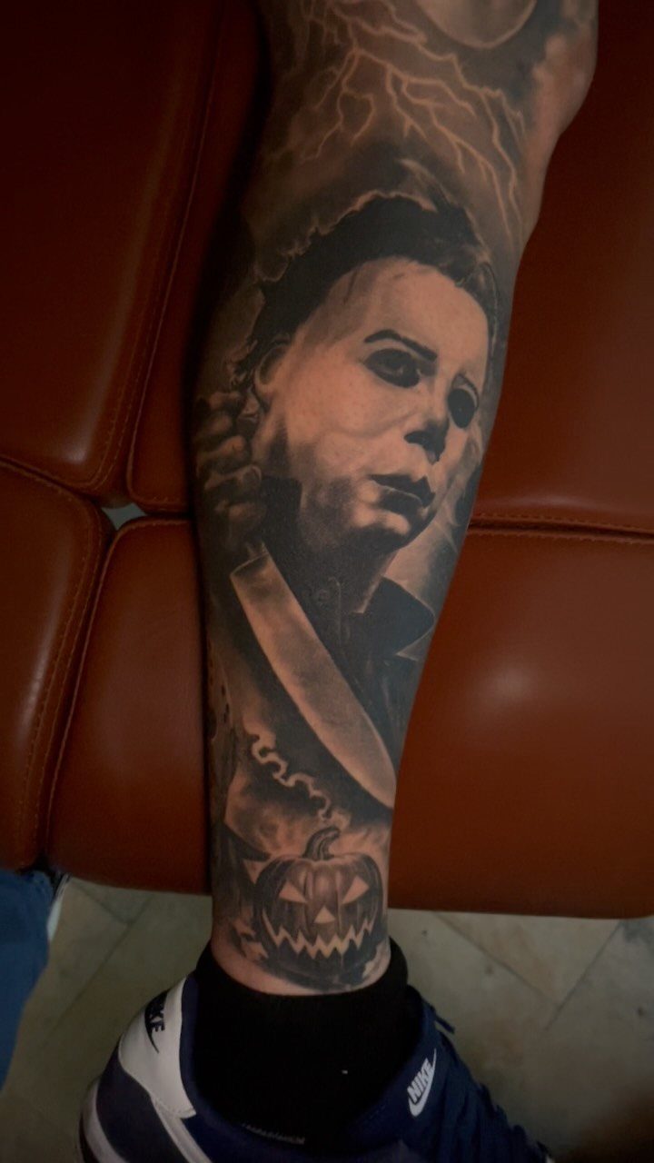 Michael Myers tattoo on a leg featuring the masked killer and a carved pumpkin.