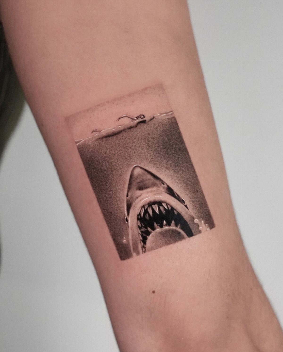 Jaws shark tattoo on an arm showing the shark's open mouth and a swimmer.