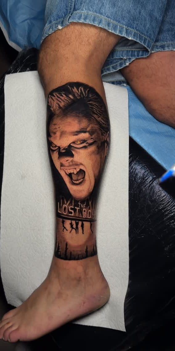 Tattoo on a lower leg depicting a screaming face and The Lost Boys text.