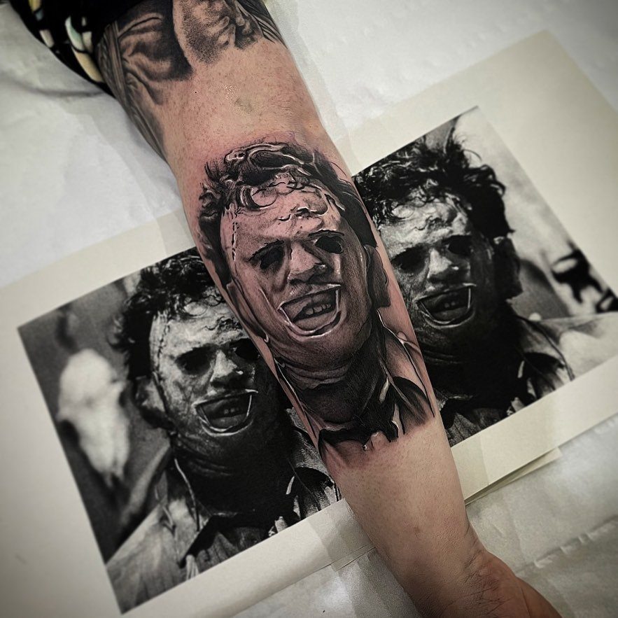 Leatherface portrait tattoo on a forearm next to a black and white reference photo