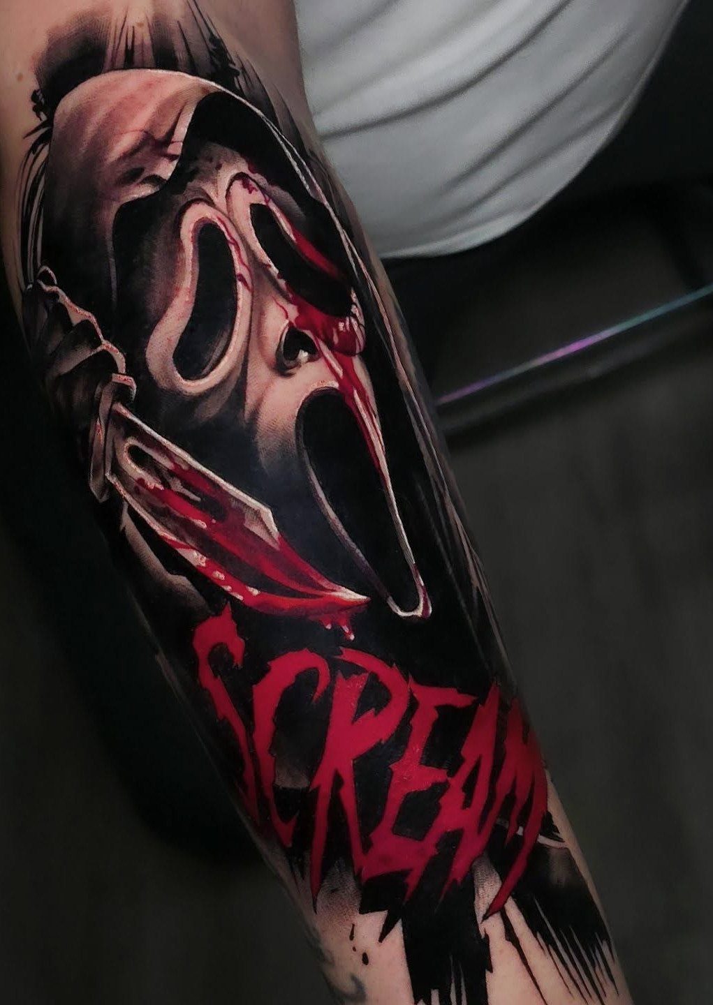 Ghostface mask tattoo with red blood and the word Scream on an arm