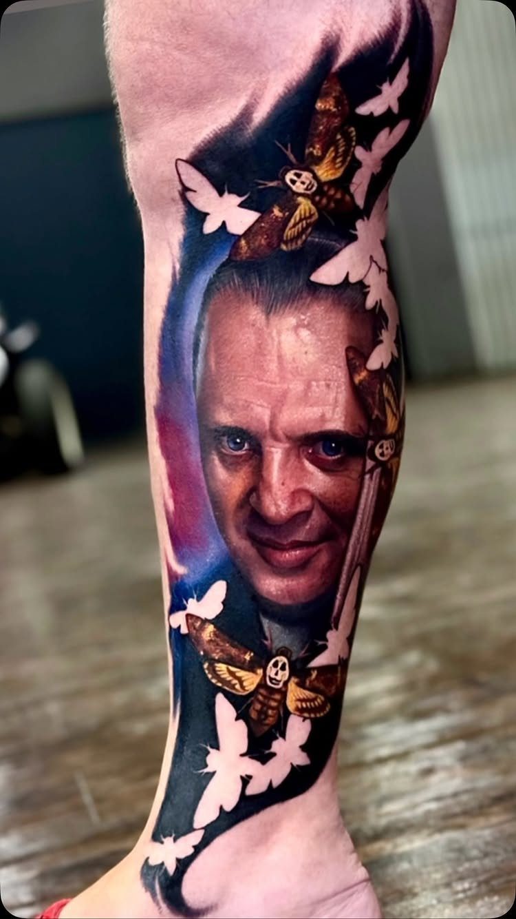 Hannibal Lecter portrait tattoo on a forearm with death's-head hawkmoths and white butterflies.