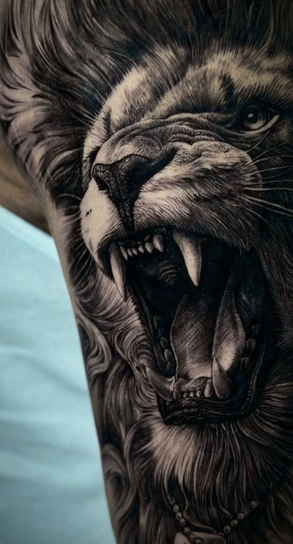 Roaring lion head tattoo with detailed fur and teeth in black and grey ink.