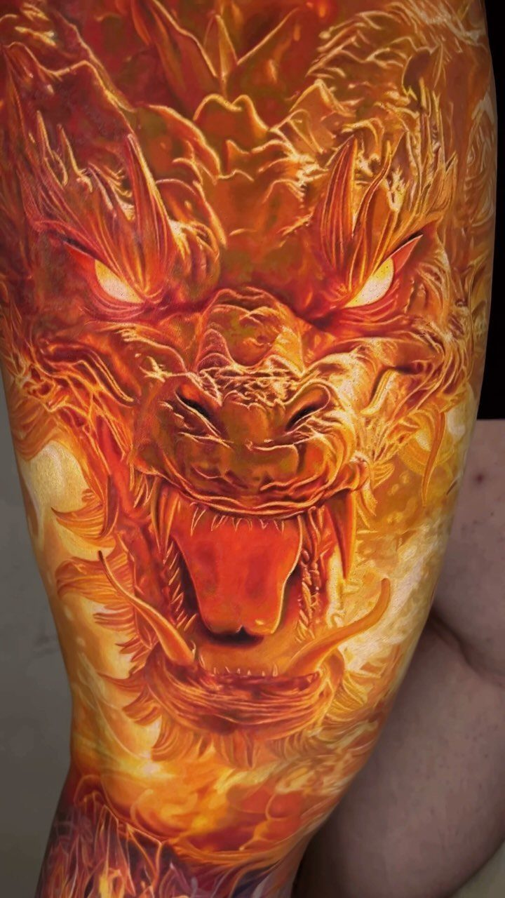 Fiery dragon head tattoo with detailed orange and yellow shading on skin.