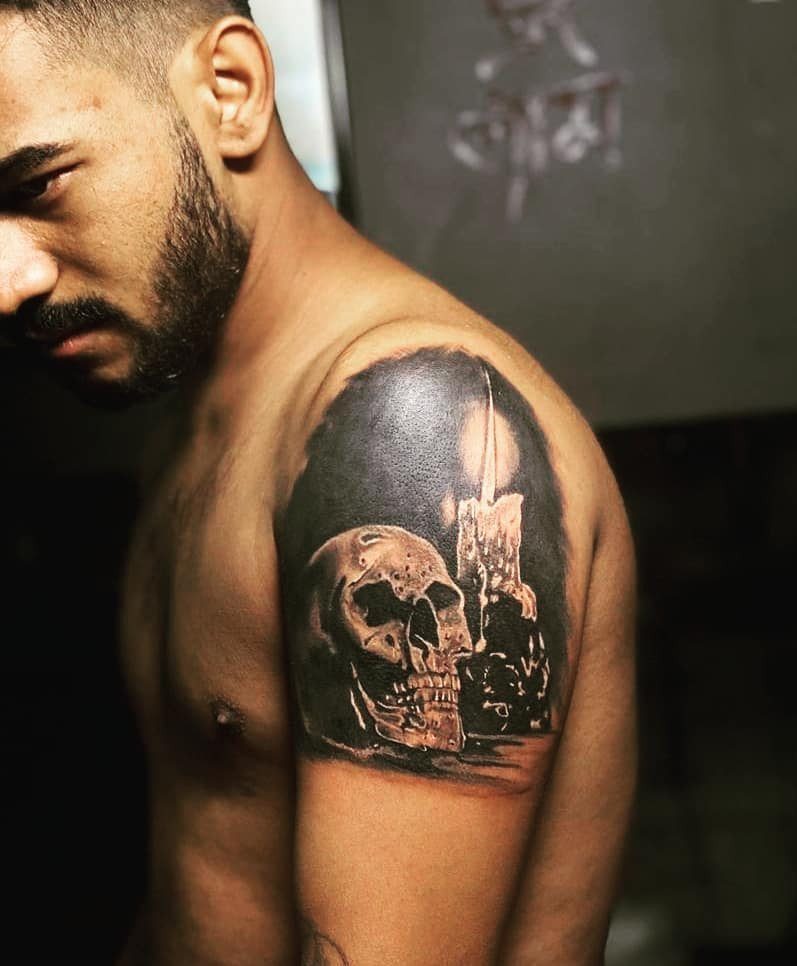 Hyper-realistic tattoo of a skull and candle on a man's upper arm.