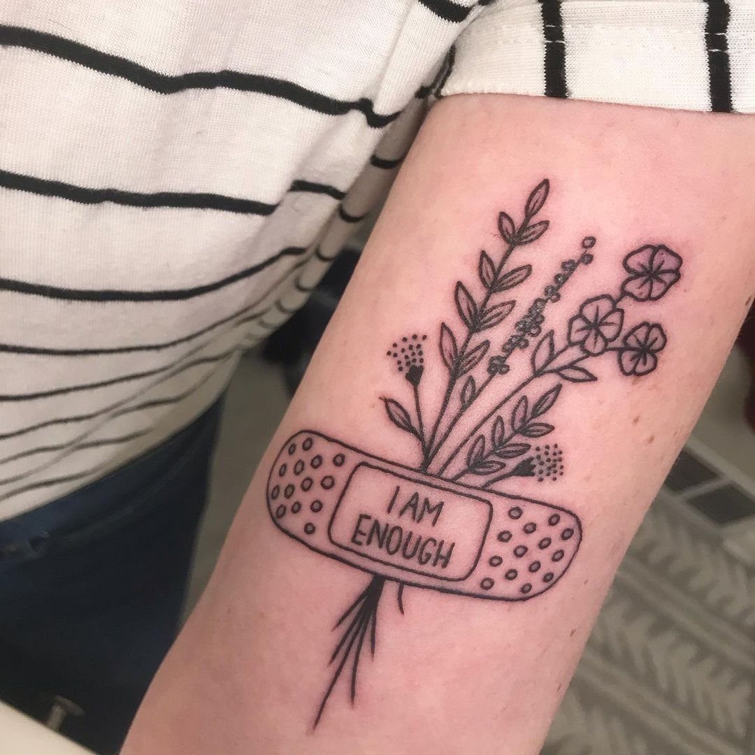 Tattoo of a bandage with I AM ENOUGH text wrapped around wildflowers