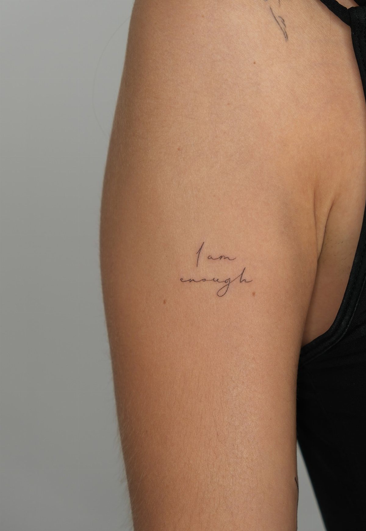 Cursive 'I am enough' tattoo on the upper arm of a person.