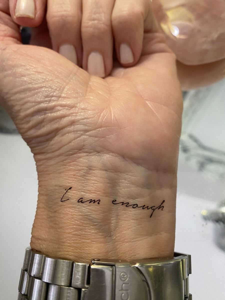 Wrist tattoo with the words I am enough written in black cursive script.